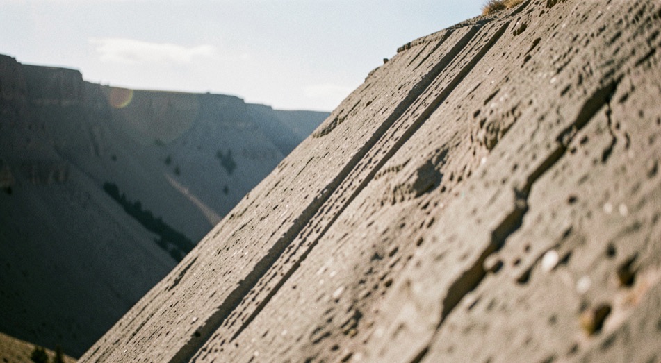A steep jump face seen from the approach in bright sun, the lip edge crisp, two parallel tire marks climbing it and stopping exactly at the crest